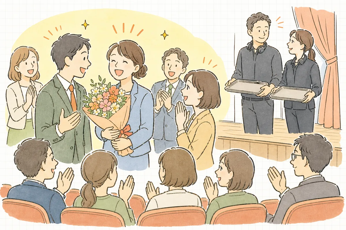 表彰式を終えた会場で、花束を抱えた受賞者が笑顔で同僚と話し、ステージ袖では制作スタッフがほっとした表情でうなずき合っている様子