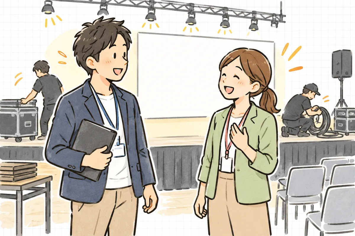 発表会が終わった会場で、片付け始めたステージを背に、主催者の担当者と笑顔で言葉を交わすイベント制作ディレクター