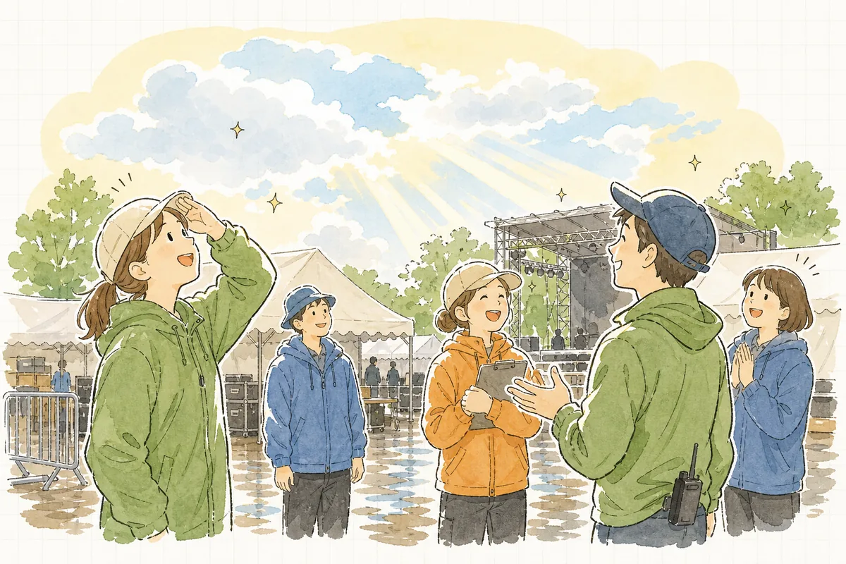 雨上がりの屋外会場で、雲の切れ間から日が差すなか、ほっとした表情で空を見上げるイベントスタッフたちの穏やかな様子